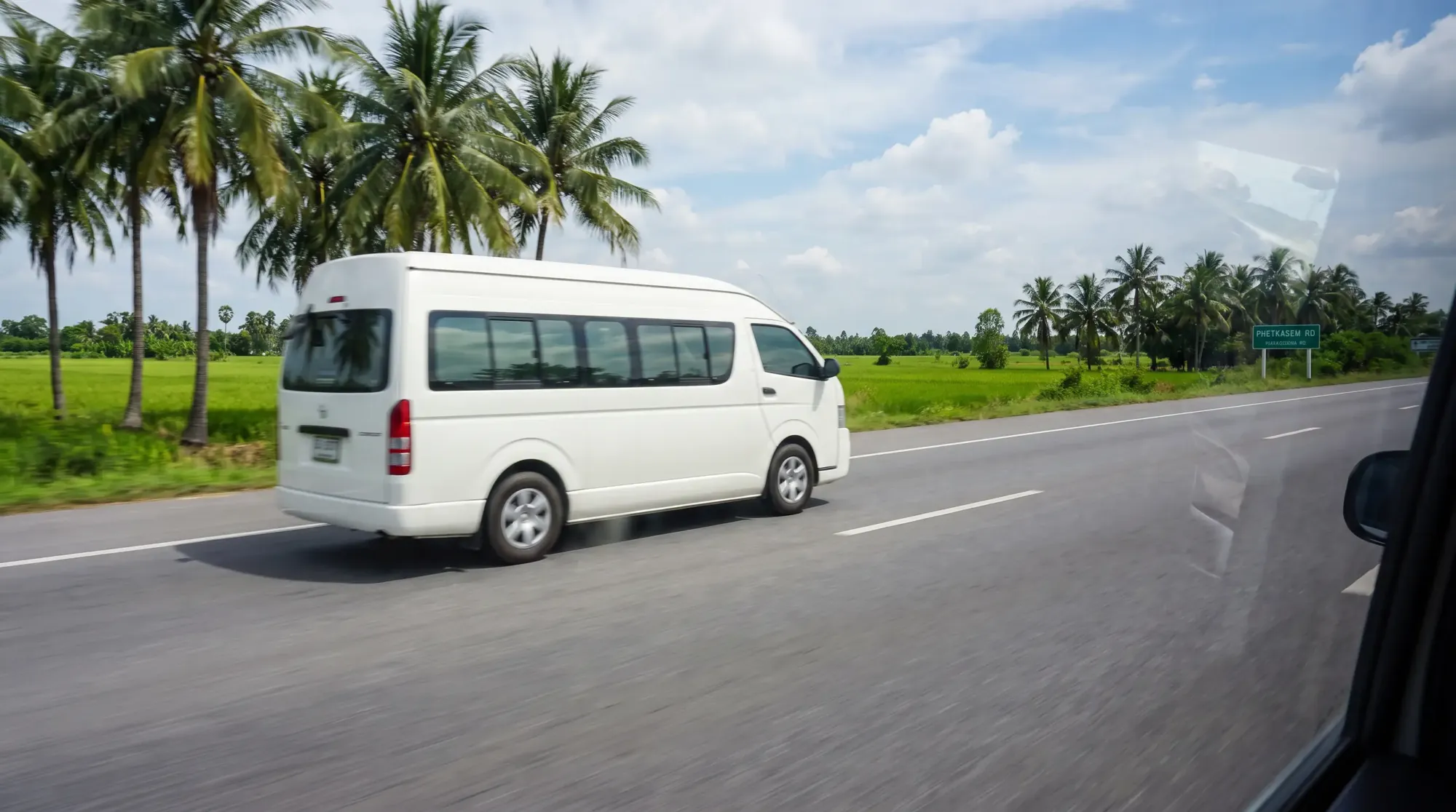 ทางหลวงหมายเลข 4 ทางใต้ของกรุงเทพฯ รถตู้ Toyota Commuter สีขาววิ่งบนถนนเรียบผ่านทุ่งเขียวและต้นมะพร้าว ฟ้าใส
